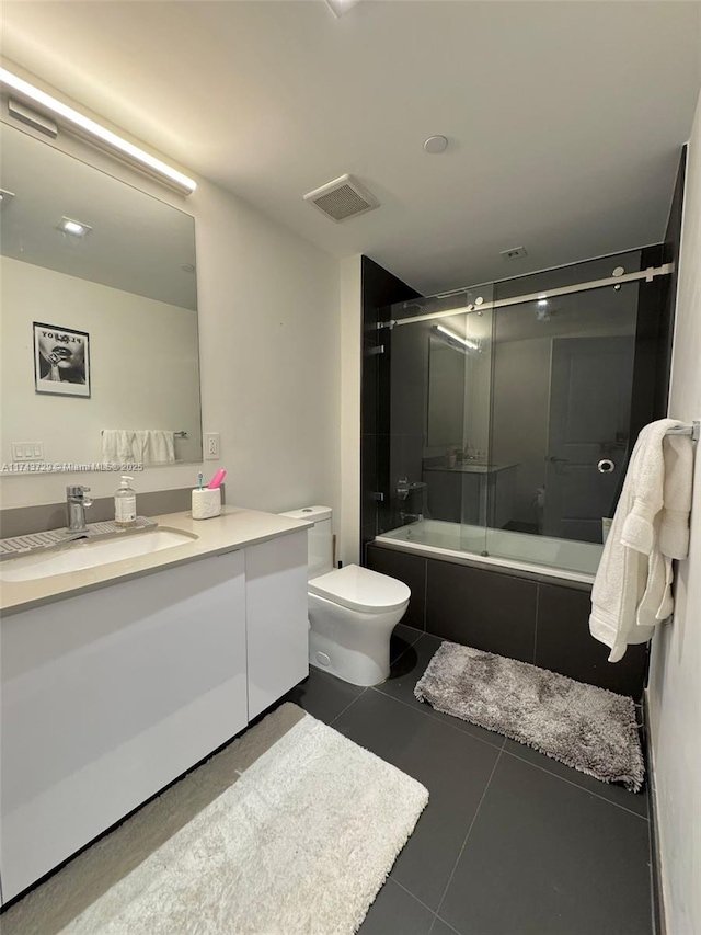 full bathroom featuring vanity, bath / shower combo with glass door, tile patterned floors, and toilet