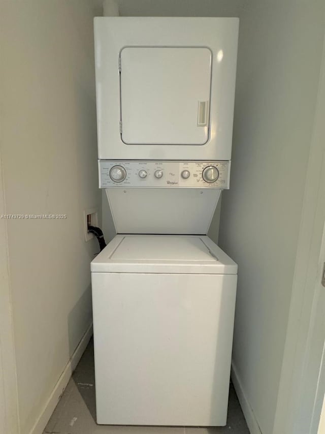 clothes washing area with stacked washer / dryer, laundry area, and baseboards