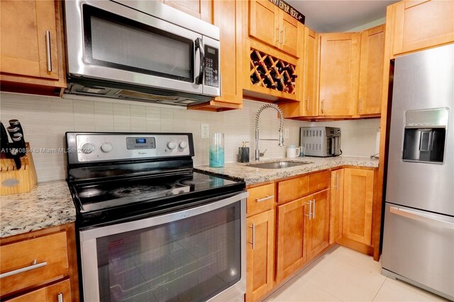 kitchen with stainless steel appliances, light stone counters, a sink, and decorative backsplash