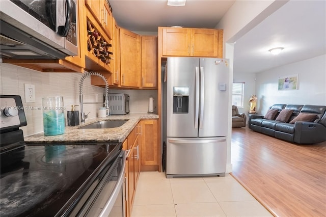 kitchen with light stone counters, stainless steel appliances, backsplash, open floor plan, and a sink