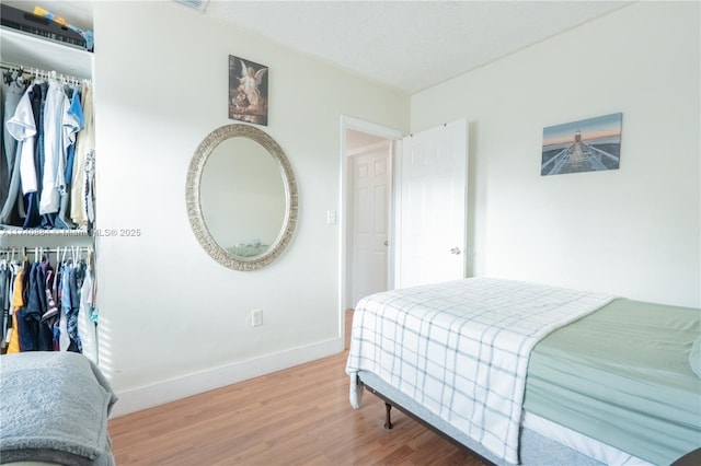 bedroom with a closet, a spacious closet, baseboards, and wood finished floors