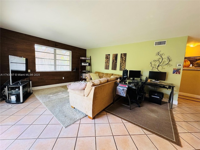 living area with light tile patterned floors, baseboards, wooden walls, and visible vents