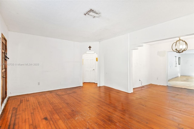 empty room with hardwood / wood-style floors and an inviting chandelier