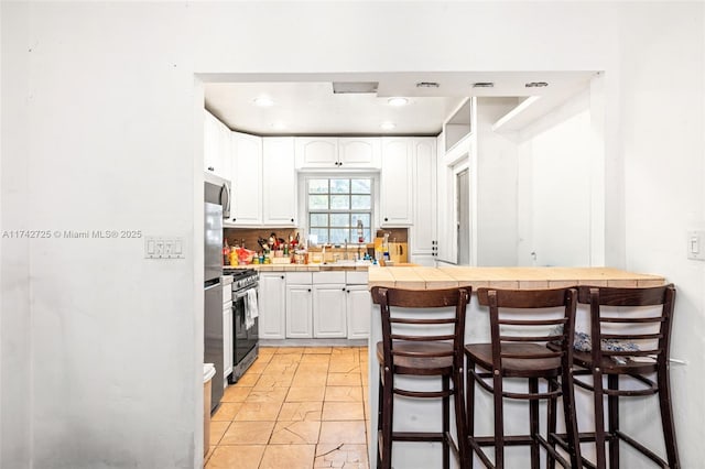 kitchen with a kitchen bar, sink, white cabinetry, tile countertops, and kitchen peninsula