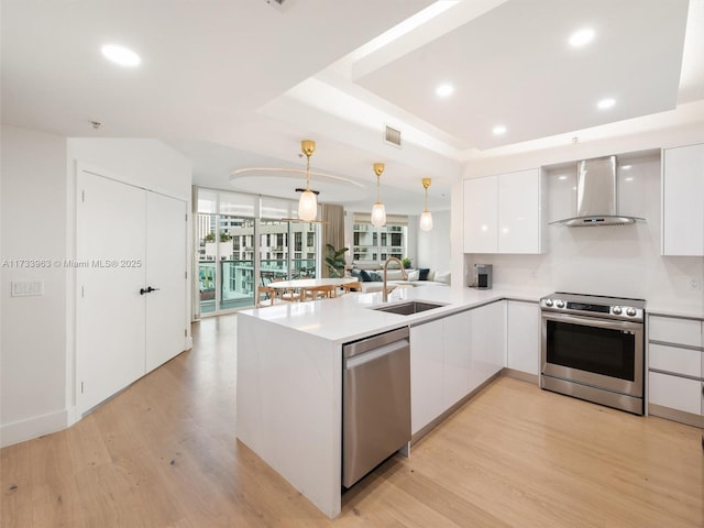 kitchen featuring white cabinetry, decorative light fixtures, kitchen peninsula, stainless steel appliances, and wall chimney range hood