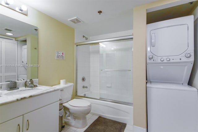 full bathroom with stacked washer and dryer, shower / bath combination with glass door, vanity, tile patterned floors, and toilet