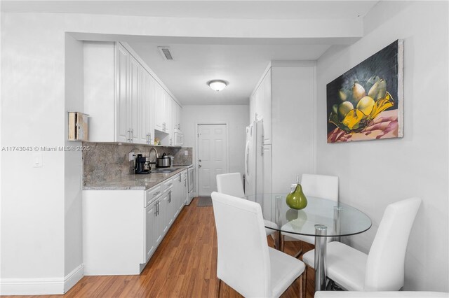 kitchen with light wood finished floors, backsplash, freestanding refrigerator, white cabinetry, and a sink
