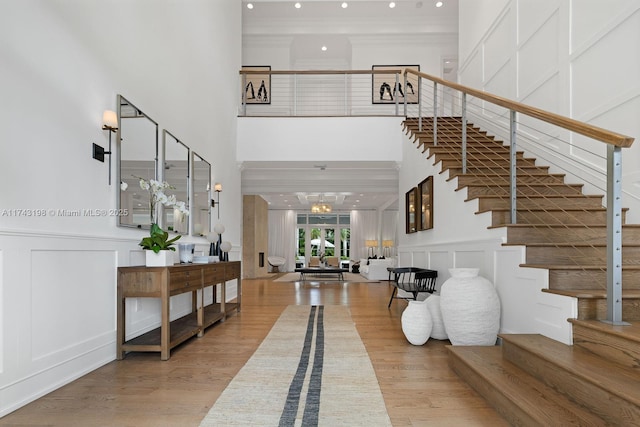 foyer with an inviting chandelier, a towering ceiling, crown molding, and hardwood / wood-style floors