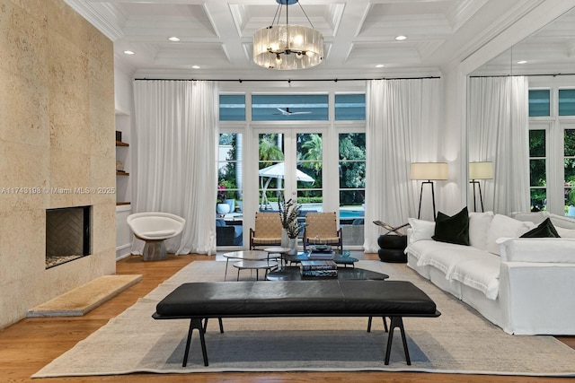 living room featuring an inviting chandelier, coffered ceiling, ornamental molding, a tiled fireplace, and light wood-type flooring