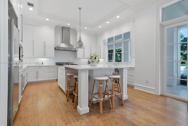 kitchen with decorative light fixtures, white cabinetry, a center island, a raised ceiling, and wall chimney exhaust hood