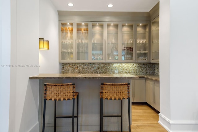 bar featuring backsplash, light hardwood / wood-style floors, and stone counters