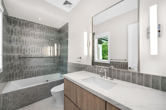 full bathroom with toilet, tiled shower / bath, tile walls, vanity, and tile patterned flooring