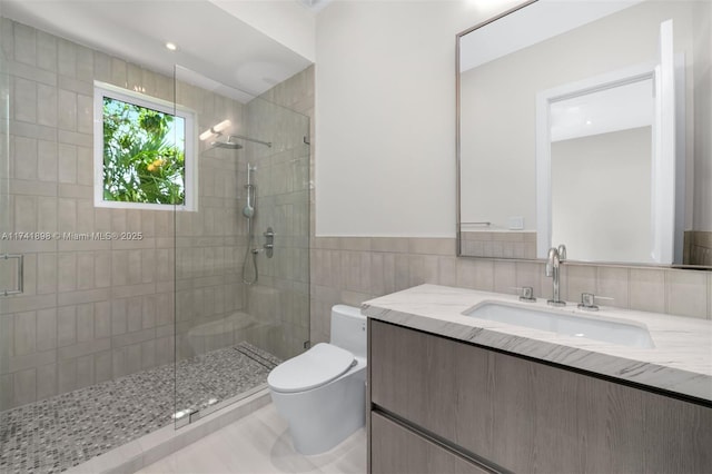 bathroom with tile walls, vanity, a shower with door, and toilet