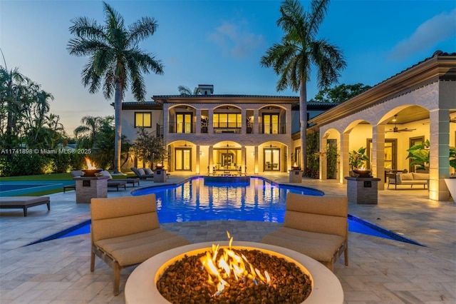 pool at dusk featuring a patio, ceiling fan, and a fire pit