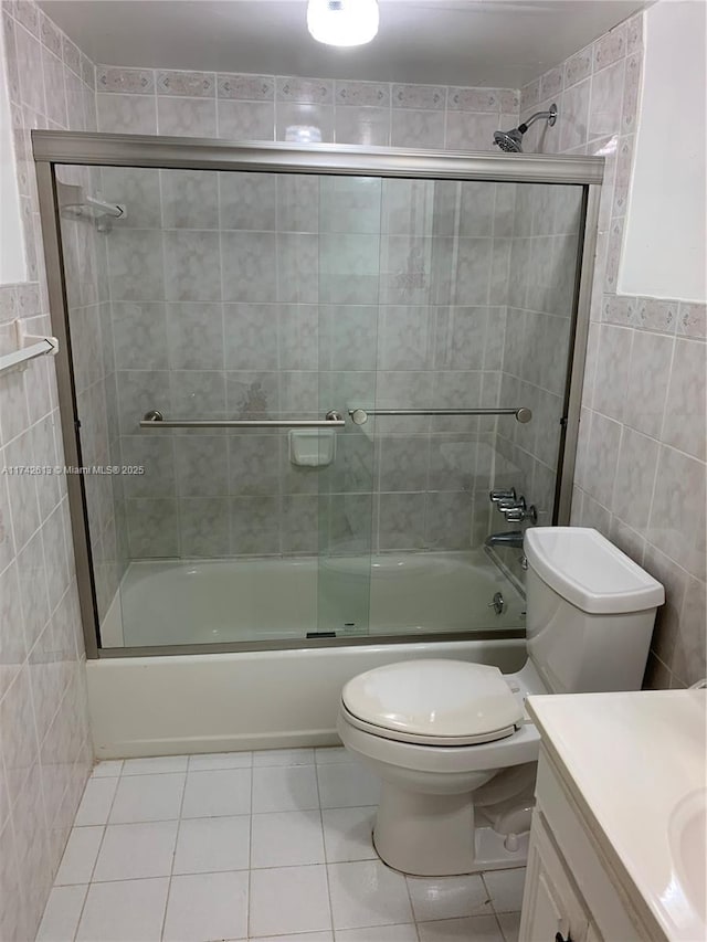 full bathroom featuring combined bath / shower with glass door, tile walls, tile patterned flooring, vanity, and toilet