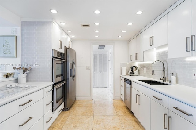 kitchen with tasteful backsplash, sink, white cabinets, light tile patterned floors, and stainless steel appliances