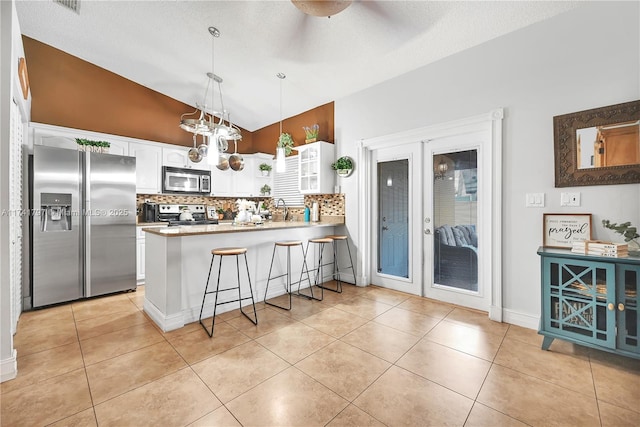 kitchen featuring light tile patterned floors, a breakfast bar, stainless steel appliances, white cabinets, and kitchen peninsula