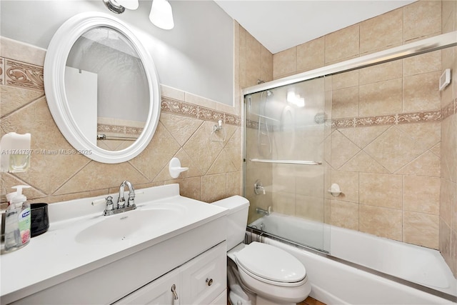 full bathroom featuring toilet, vanity, bath / shower combo with glass door, and tile walls