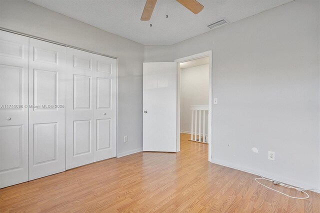 unfurnished bedroom featuring ceiling fan, a textured ceiling, light wood-style flooring, visible vents, and a closet