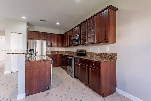 kitchen featuring sink, appliances with stainless steel finishes, dark stone countertops, a center island, and light tile patterned flooring