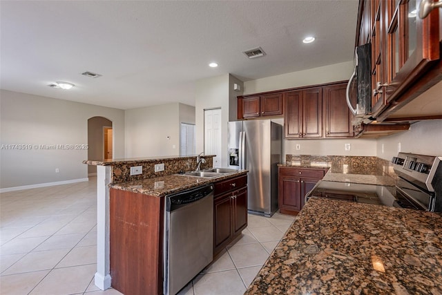 kitchen with sink, dark stone countertops, a kitchen island with sink, light tile patterned floors, and stainless steel appliances