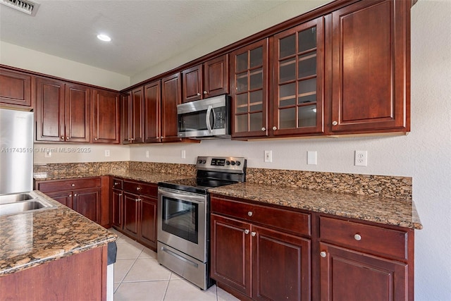 kitchen featuring light tile patterned flooring, sink, a textured ceiling, dark stone counters, and stainless steel appliances