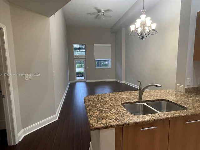 kitchen with decorative light fixtures, sink, dark hardwood / wood-style flooring, dark stone counters, and kitchen peninsula