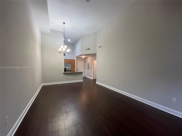 unfurnished living room featuring high vaulted ceiling, an inviting chandelier, and dark hardwood / wood-style flooring