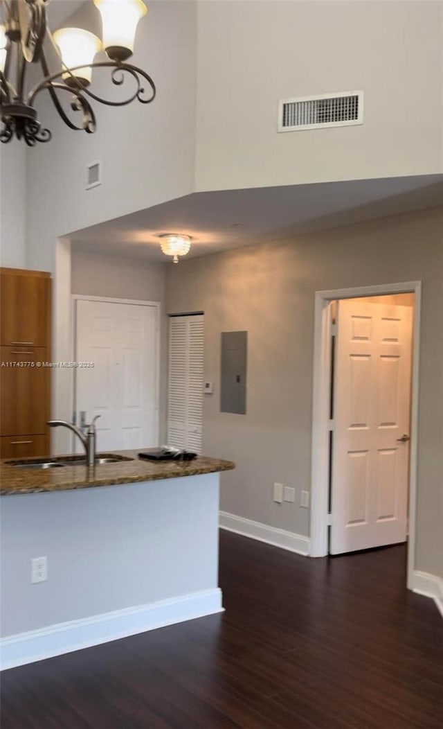 kitchen with dark wood-type flooring, sink, electric panel, a notable chandelier, and a towering ceiling