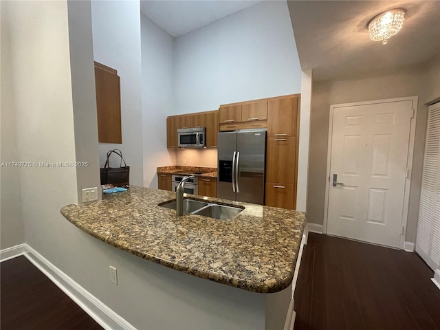 kitchen featuring appliances with stainless steel finishes, sink, dark stone countertops, kitchen peninsula, and dark wood-type flooring