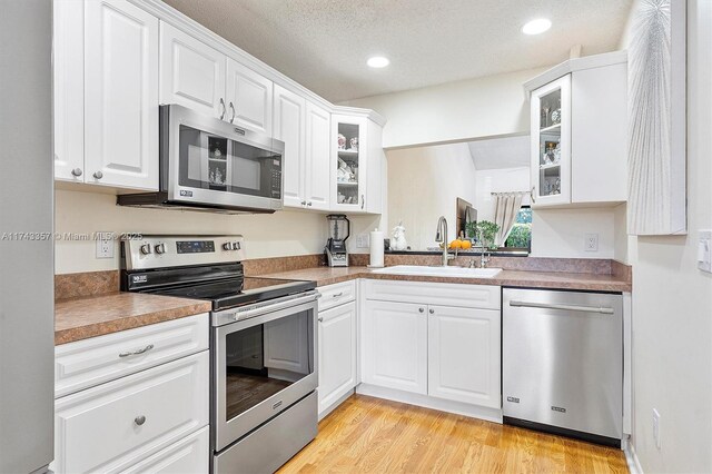 4149 S Pine Island Rd, Davie, FL 33328 - kitchen with stainless steel appliances, glass insert cabinets, white cabinetry, a sink, and light wood-style floors