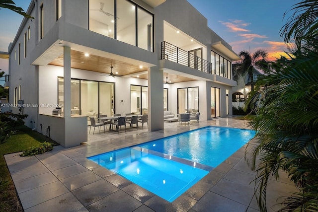 back house at dusk with a swimming pool with hot tub, a balcony, ceiling fan, and a patio area