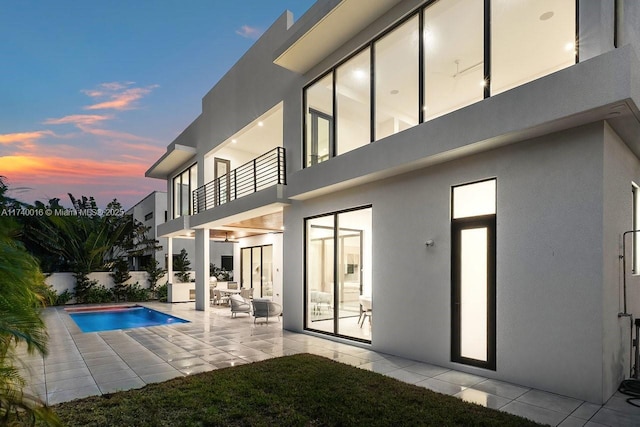 back house at dusk with a fenced in pool, a patio, and a balcony