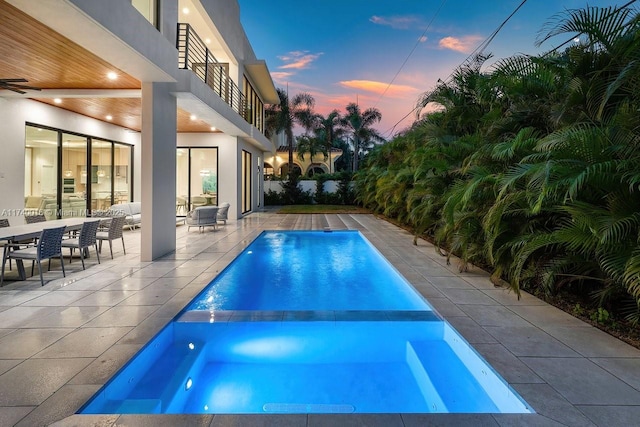 pool at dusk with outdoor lounge area and a patio