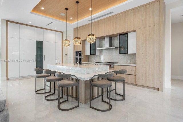 kitchen featuring wall chimney range hood, wood ceiling, hanging light fixtures, a tray ceiling, and white cabinets