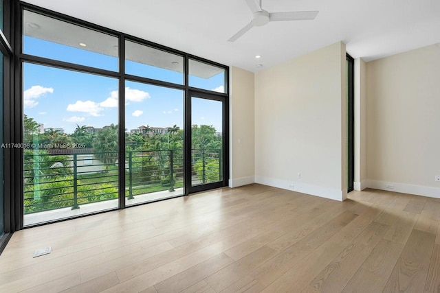 unfurnished room with ceiling fan, a wall of windows, and light wood-type flooring