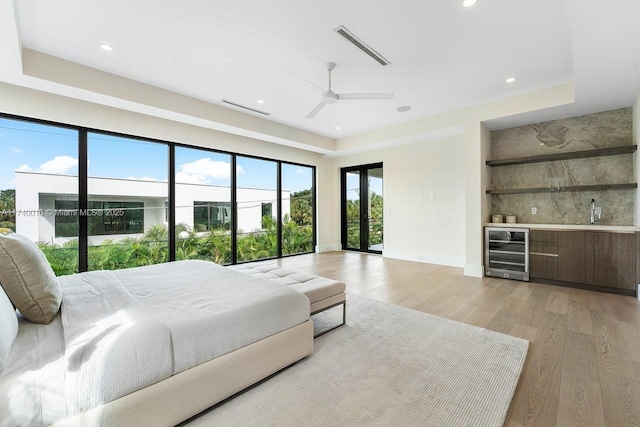 bedroom featuring indoor bar, beverage cooler, access to exterior, ceiling fan, and light hardwood / wood-style floors