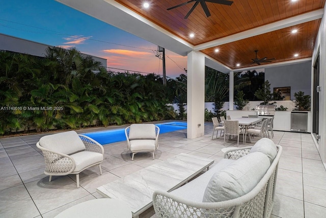 patio terrace at dusk featuring ceiling fan and an outdoor kitchen