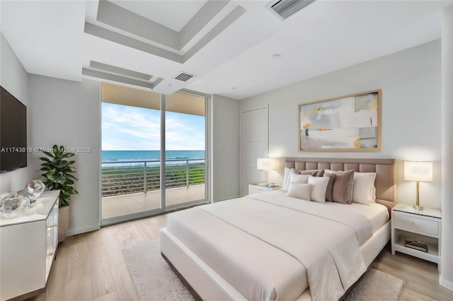 bedroom with a water view, expansive windows, access to outside, a raised ceiling, and light wood-type flooring