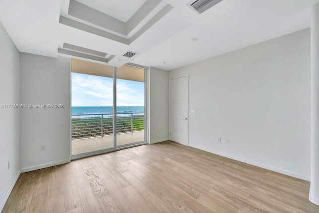 empty room featuring a water view, floor to ceiling windows, a raised ceiling, and light hardwood / wood-style floors