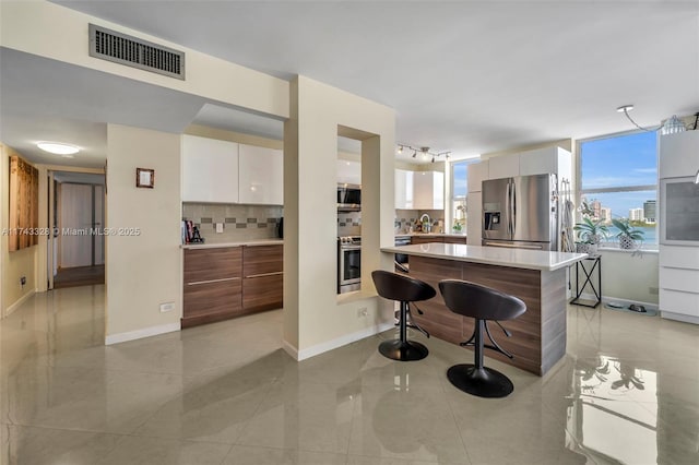 kitchen with white cabinetry, a kitchen breakfast bar, a kitchen island, stainless steel appliances, and decorative backsplash