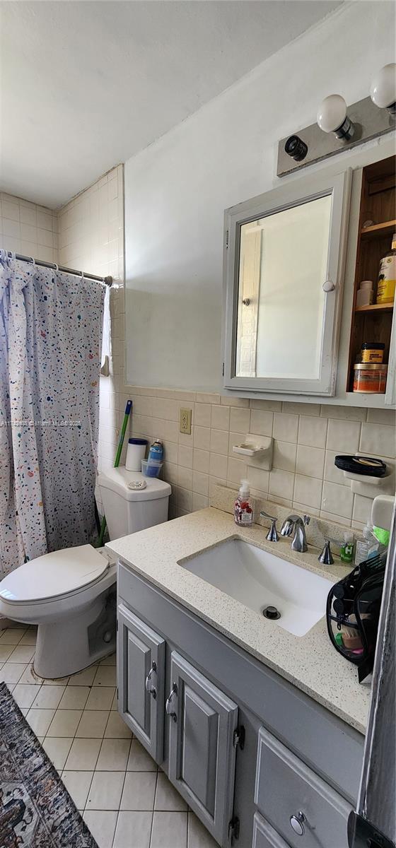 bathroom featuring tile walls, vanity, tile patterned floors, toilet, and walk in shower