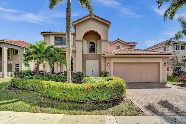 mediterranean / spanish-style house with a garage, a tile roof, decorative driveway, and stucco siding