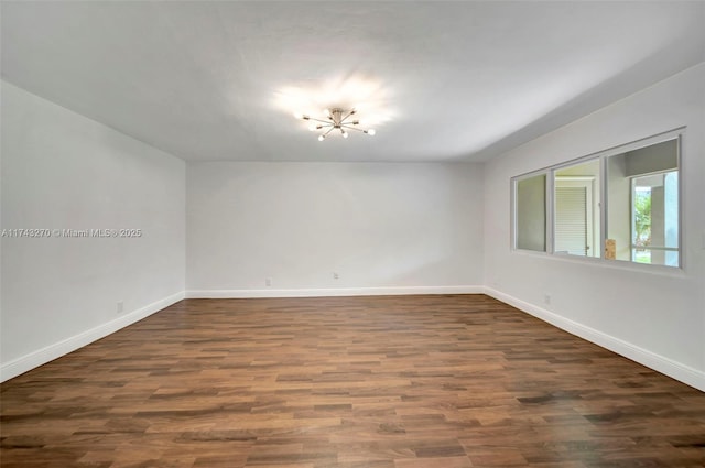 empty room with dark hardwood / wood-style flooring and a notable chandelier