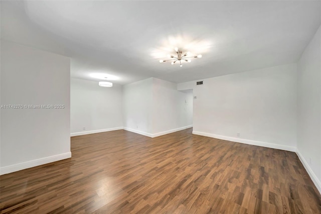 empty room with dark wood-type flooring and an inviting chandelier