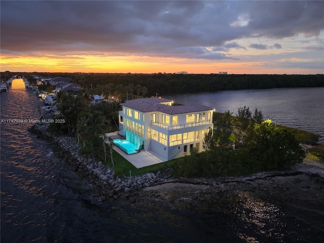 back of house at dusk with a balcony and a water view