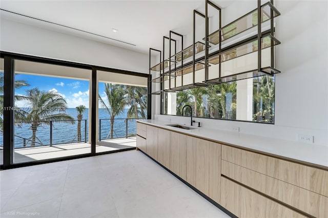 kitchen with a water view, light brown cabinetry, light countertops, modern cabinets, and a sink