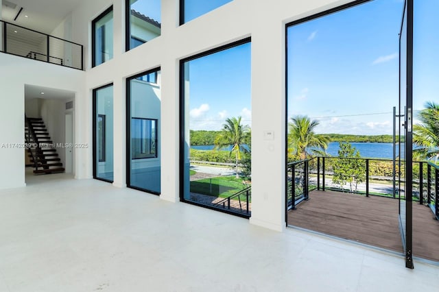 unfurnished room featuring a water view, a high ceiling, a healthy amount of sunlight, and stairs