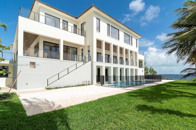 rear view of house featuring an outdoor pool, stucco siding, a water view, a tiled roof, and a lawn