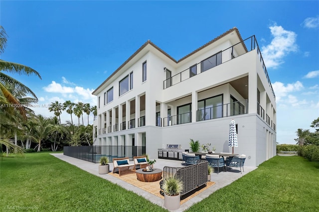 rear view of property featuring stucco siding, a patio, a lawn, and an outdoor living space with a fire pit